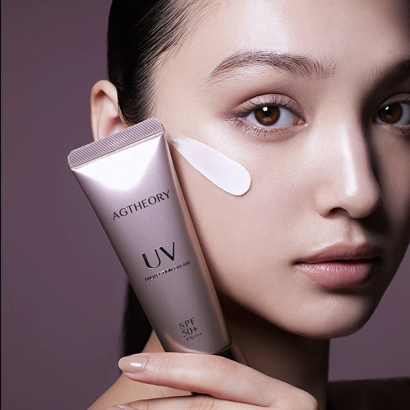 A model holding AGTHEORY UV Protection Cream with cream on her cheek